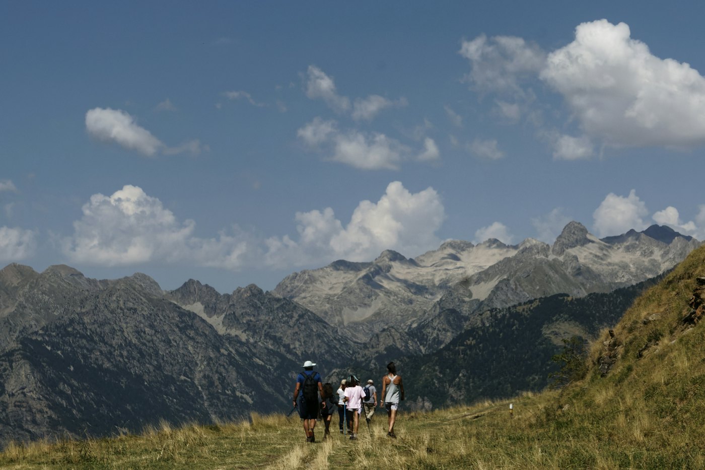 A group of friends walking along a grassy ridge towards rocky peaks