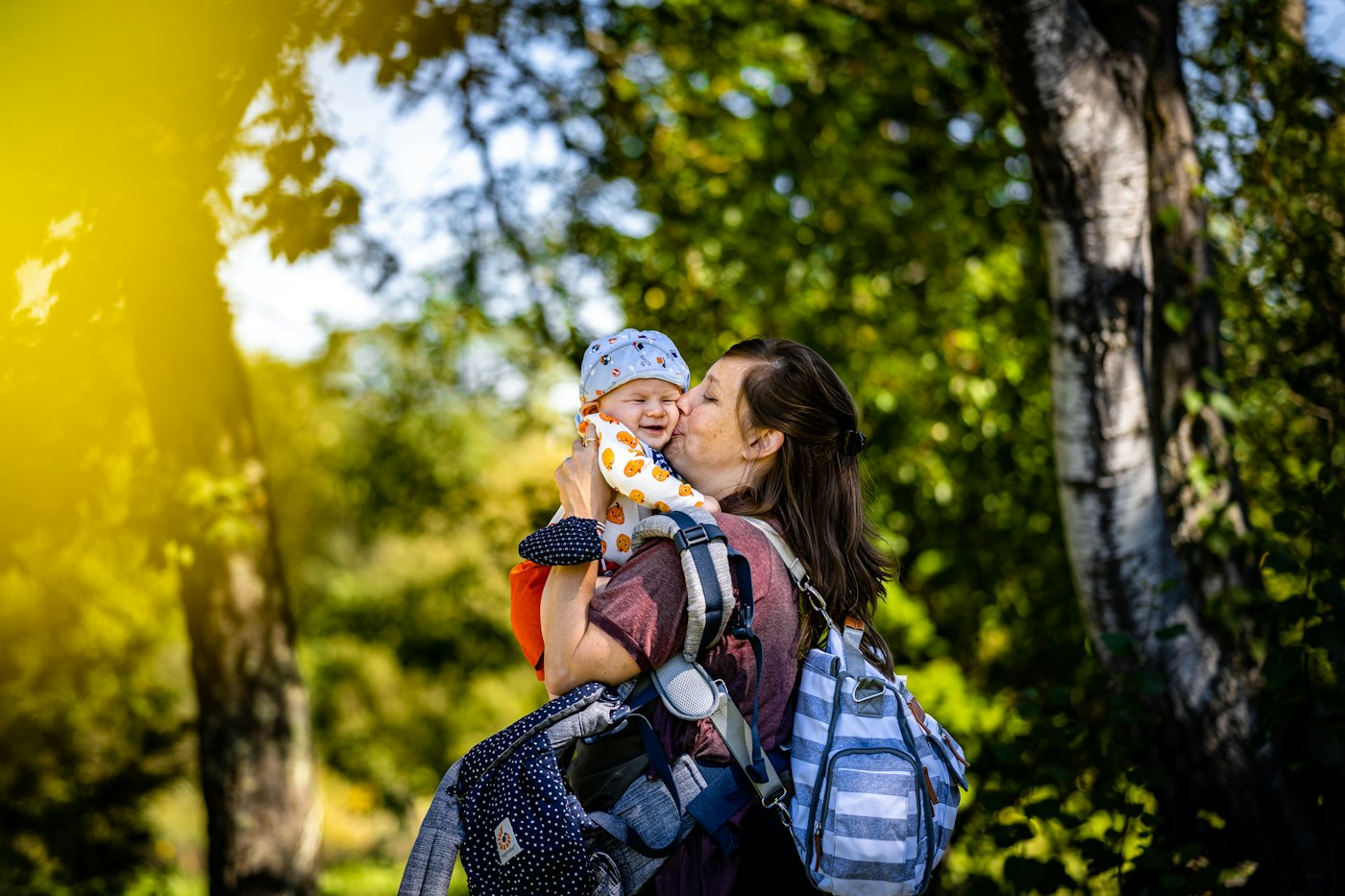 A mother kissing her laughing baby in a sunny birch wood