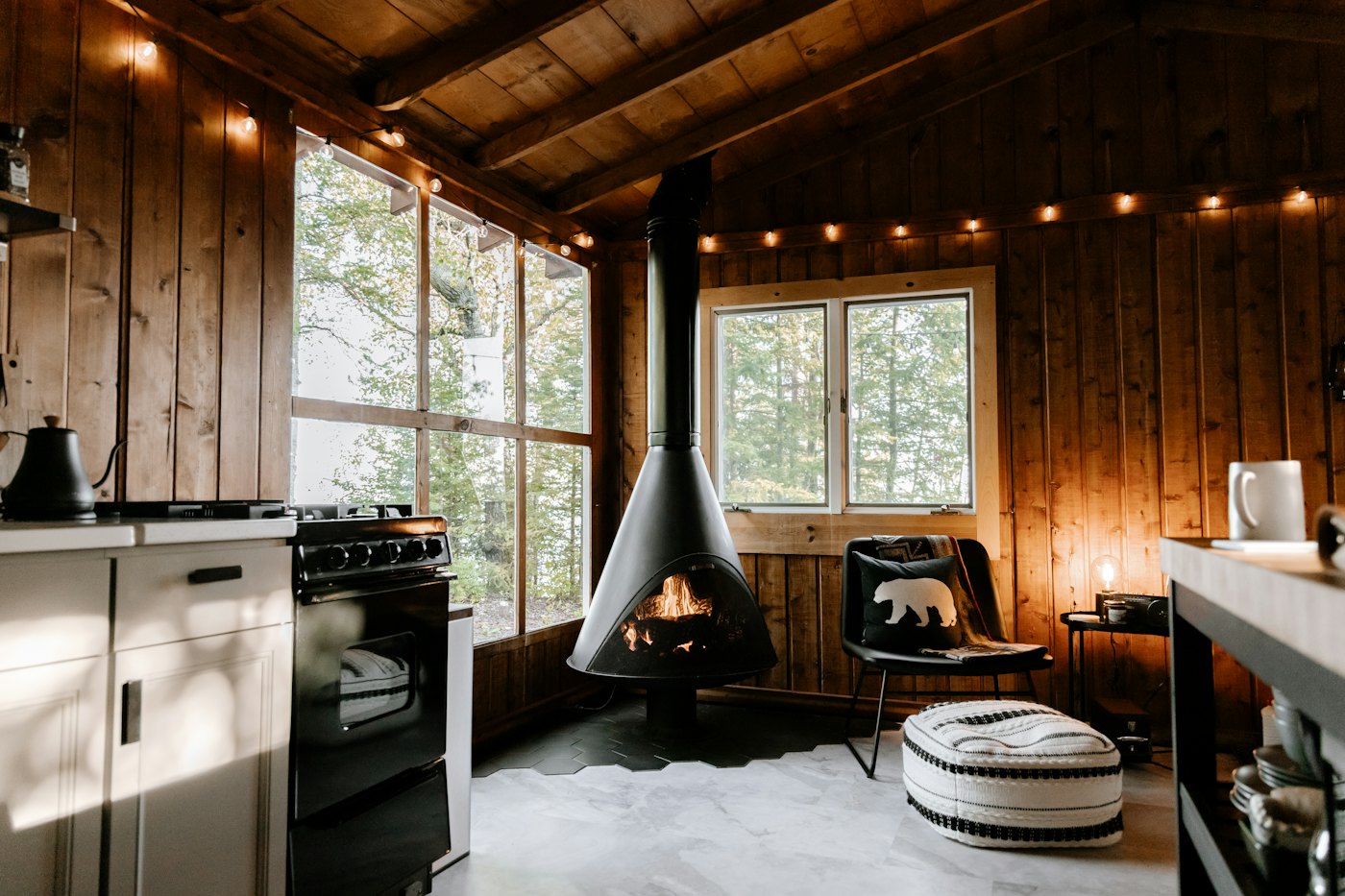 Timber-walled studio with a black cone wood stove, armchair and small kitchen