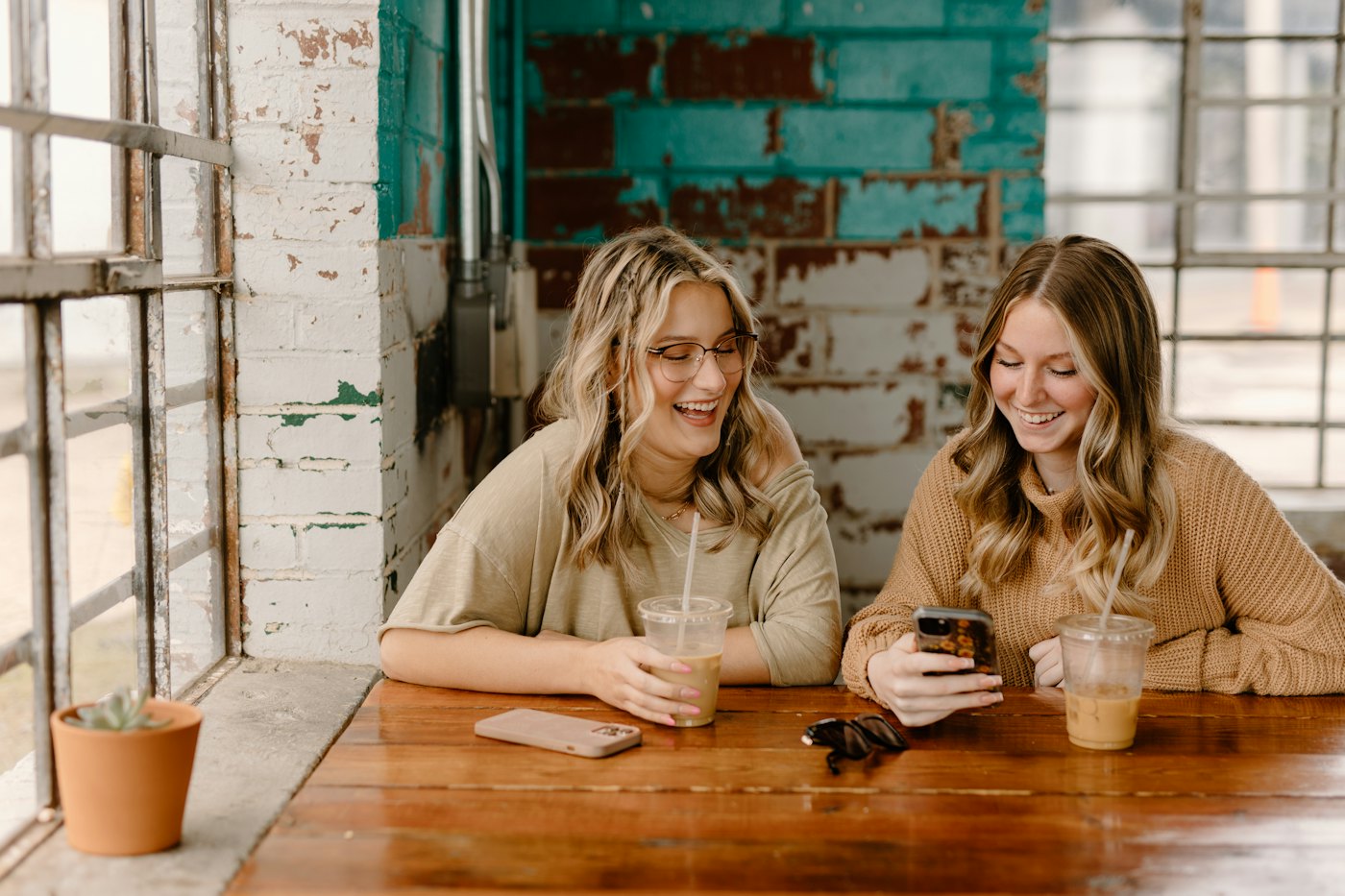 Two friends at a café table looking at a phone together