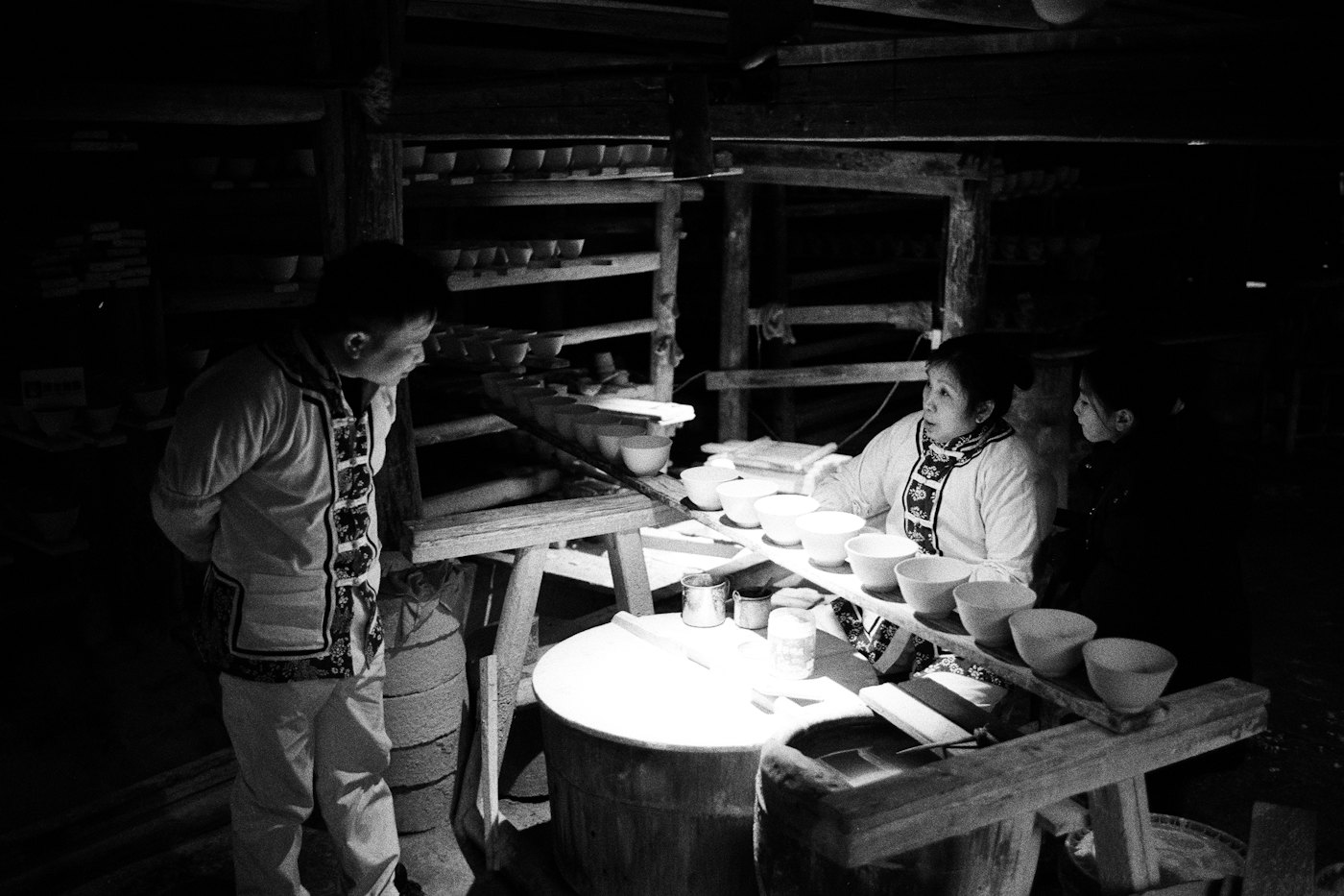 Three people shaping pottery in a dimly lit workshop